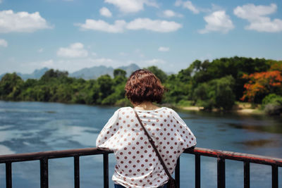 Rear view of woman standing by railing against sea