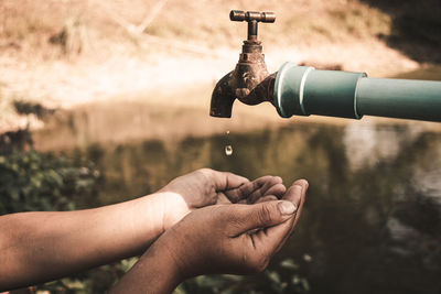 Close-up of hand holding faucet against water