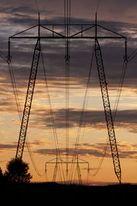 Silhouette electricity pylon on field against sky at sunset