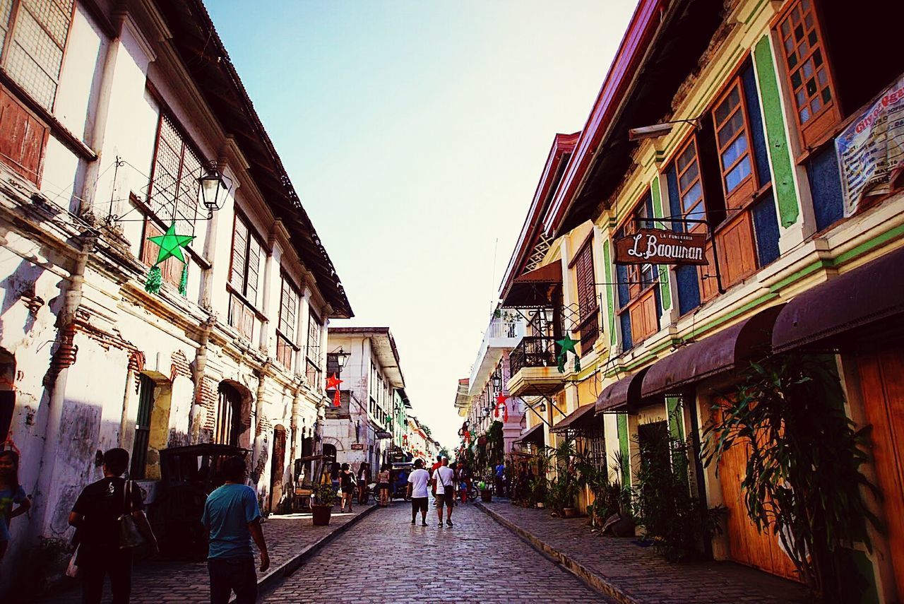 PEOPLE WALKING ON STREET AMIDST BUILDINGS IN CITY