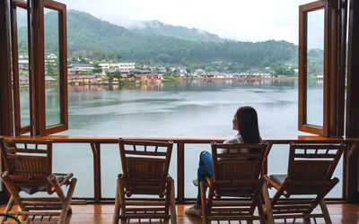 A young woman sitting on balcony and looking at a beautiful lake in mountains village