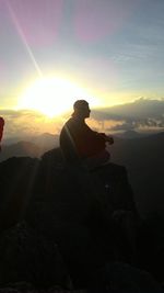 Man sitting on rock against sky during sunset