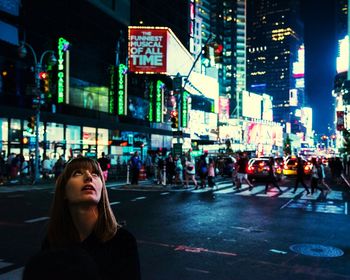 Close-up of young woman looking up while standing at times square during night