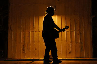 Side view of silhouette man standing against wall at night