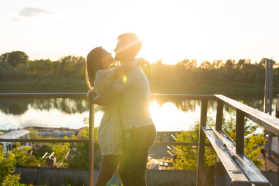 Couple standing on railing by lake against sky