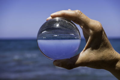 Cropped hand of person holding crystal ball against sea