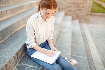 Woman holding book while sitting on steps