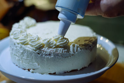 Person prepairing cake with whipped cream on table