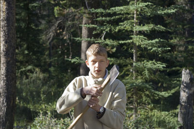 Portrait of boy holding axe while standing against trees at jasper national park
