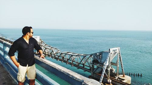 Man standing on railing against sea