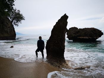 Man standing on rock by sea against sky