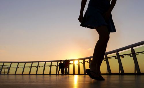 Low section of woman with children in background at observation point during sunset