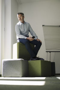 Businessman looking away while sitting on heap of hassock at office