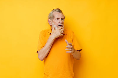 Portrait of young woman holding hands against yellow background