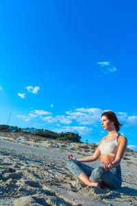 Side view of woman sitting on land against blue sky