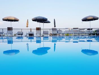 Reflection of umbrellas and lounge chairs in swimming pool against clear sky