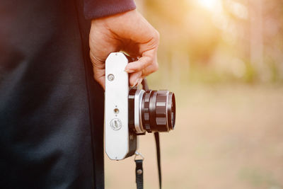 Midsection of man holding camera while standing outdoors