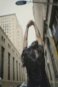 Rear view of woman with arms raised standing in city