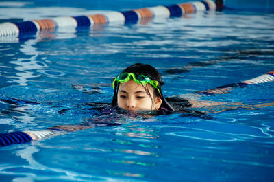 Closeup portrait of cute little peruvian girl swimming in the pool, happy child having fun in water