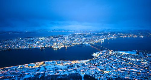 High angle view of illuminated city by sea against blue sky