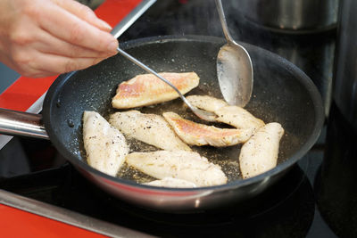 Cropped hand frying mullet fish in pan