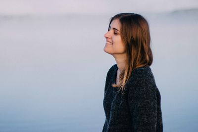 Side view of smiling young woman standing against lake