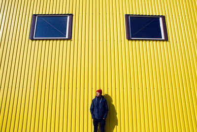 Guy in the red hat stands at the wall of the iron house in nature next to the lake