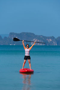 Young sporty woman playing stand-up paddle board on the blue sea in sunny day of summer vacation