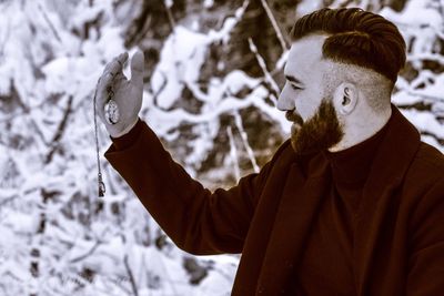 Young man holding pocket watch during winter