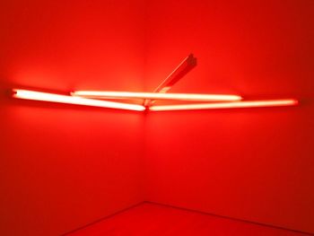 Low angle view of illuminated fluorescent lights on red wall