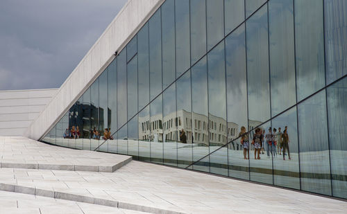 People reflecting on modern building against sky