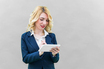 Young woman using phone while standing against white background