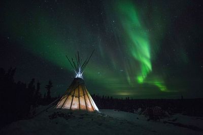 Illuminated tent against aurora borealis in sky at night