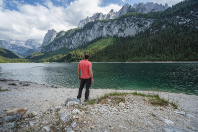 Rear view of man standing on mountain by lake