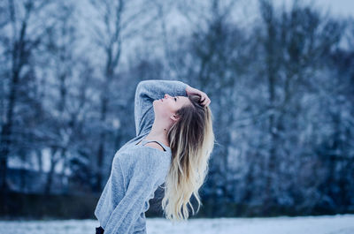 Side view of young woman standing against bare trees during winter