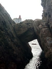 Rock formation by sea and buildings against sky