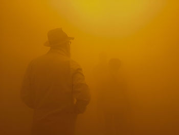 Rear view of man standing against orange sky during foggy weather