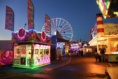 People in illuminated amusement park against sky at night