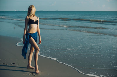 Portrait of young woman standing at beach against sky