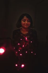 Portrait of smiling woman standing against illuminated christmas lights