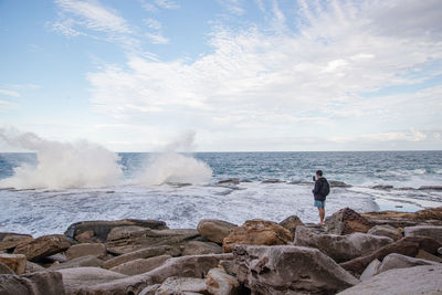 Man standing on rocks by sea against sky