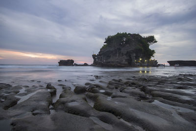 Rock formation on sea against cloudy sky during sunset