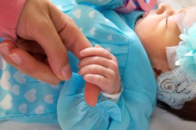 Close-up of newborn baby girl holding mother finger while sleeping in hospital