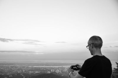 Rear view of man looking at cityscape against sky