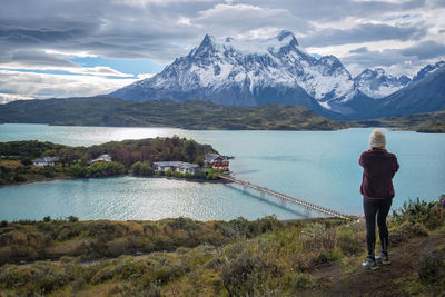 Rear view of man standing on mountain by lake against sky