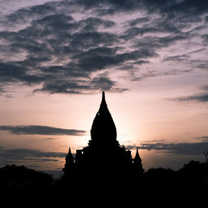 Silhouette of temple building against cloudy sky