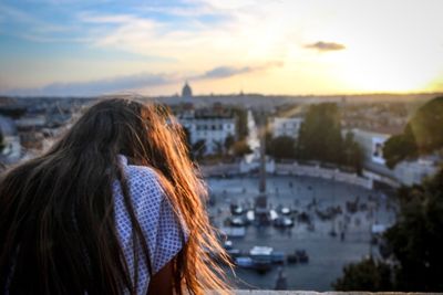 Rear view of woman looking at cityscape against sky