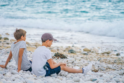 Two boys sitting next to each other on the beach by the sea