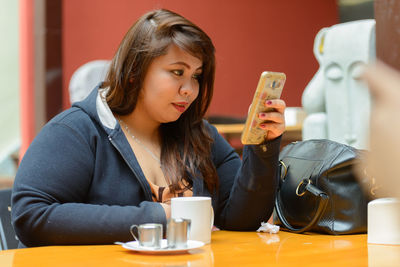 Young woman using mobile phone while sitting on table