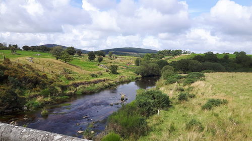 Stream by land against cloudy sky